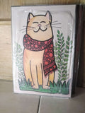 Cuadro ilustración gato crema sonriente con bufanda lunares rojos entre plantas verdes madera 19x28 cm